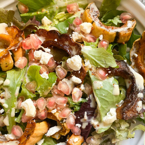 A flatlay image of roast delicata squash slices tossed with seasonal greens, pomegranate seeds, and more for this Maple Roast Delicata Squash Salad.