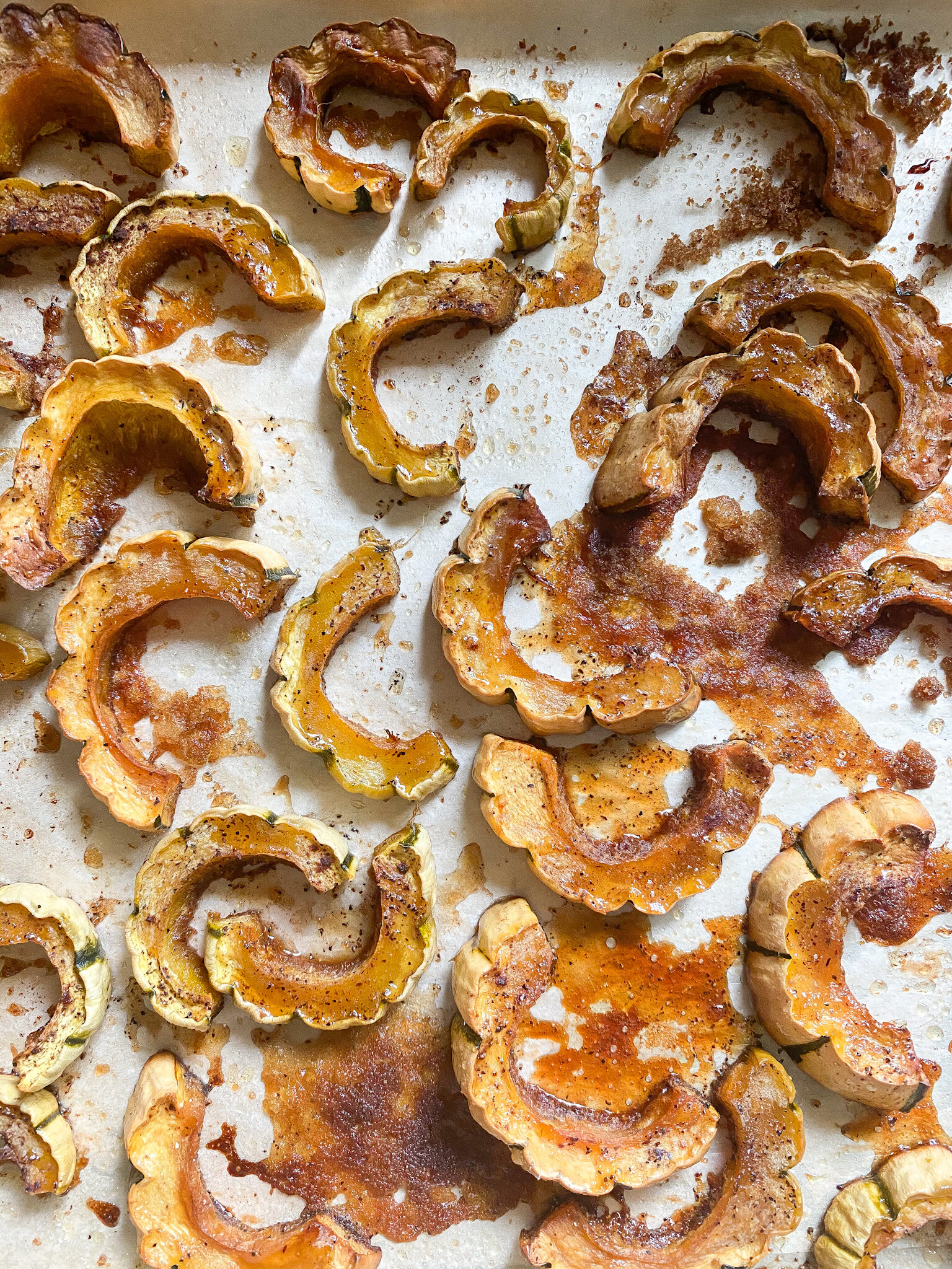 A rimmed baking sheet shows freshly roasted delicata squash tossed in a maple glaze.