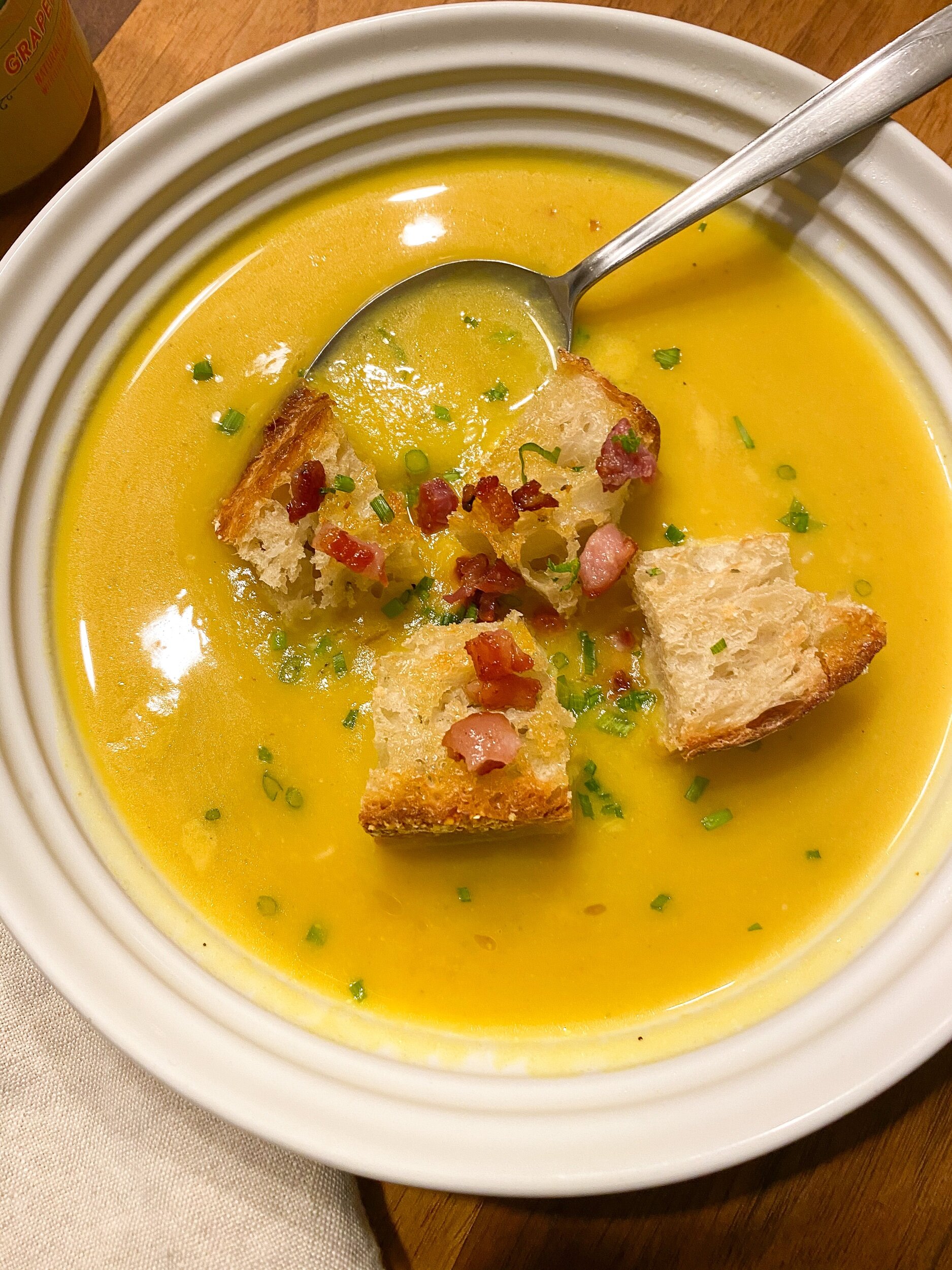 A white soup bowl contains a delicious bowl of Roast Dumpling Squash Soup with Crispy Pancetta and Croutons.