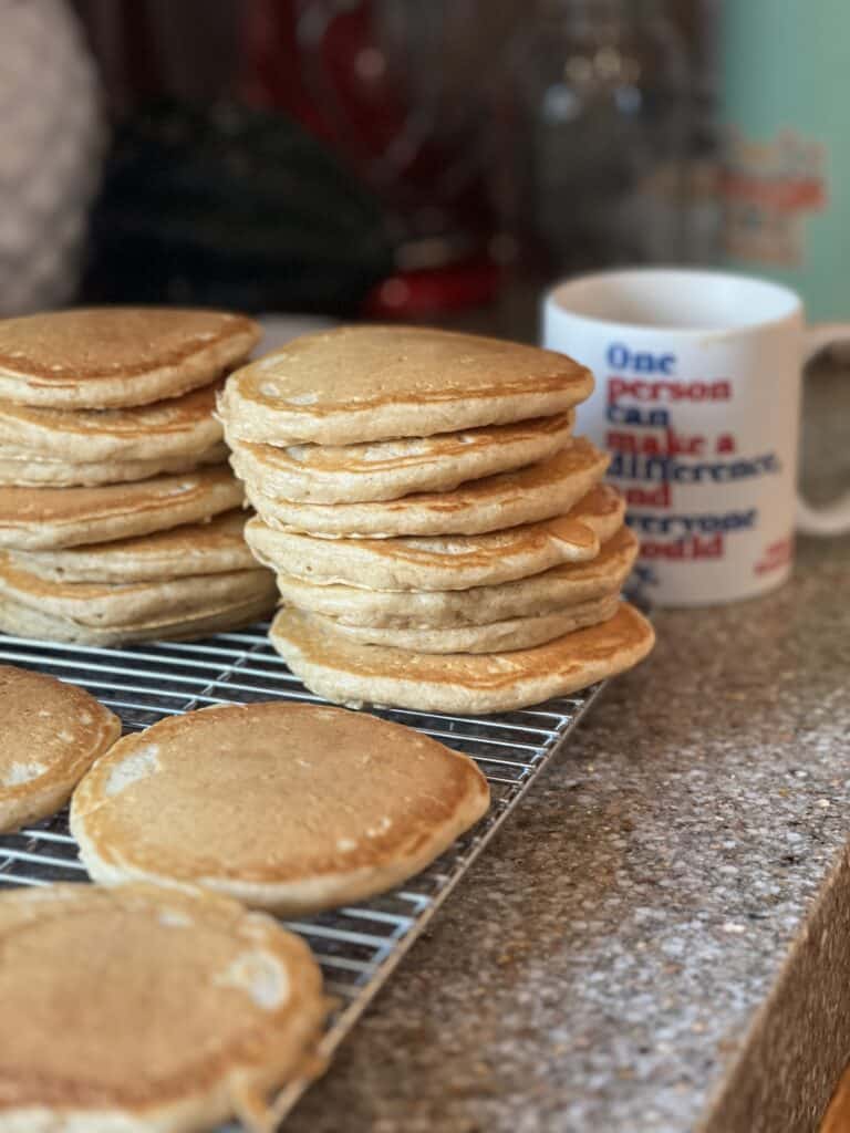 Portrait shot of a stack of pancakes during Sunday morning pancake prep. Edges are golden brown and pancakes are stacked about 7 pancakes high on a wire cooling rack. 