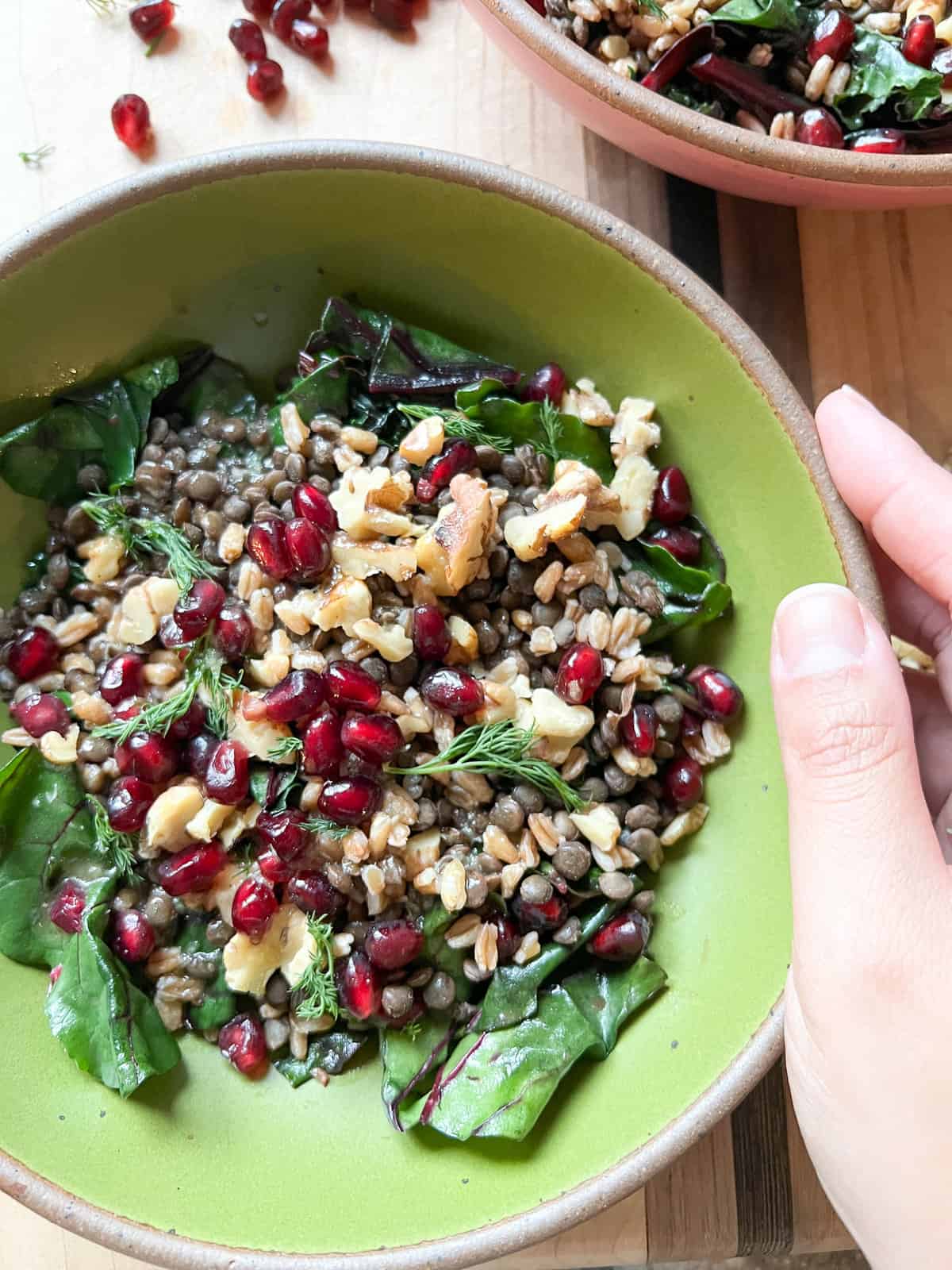 a bowl of grains and greens adorned with pomegranate seeds