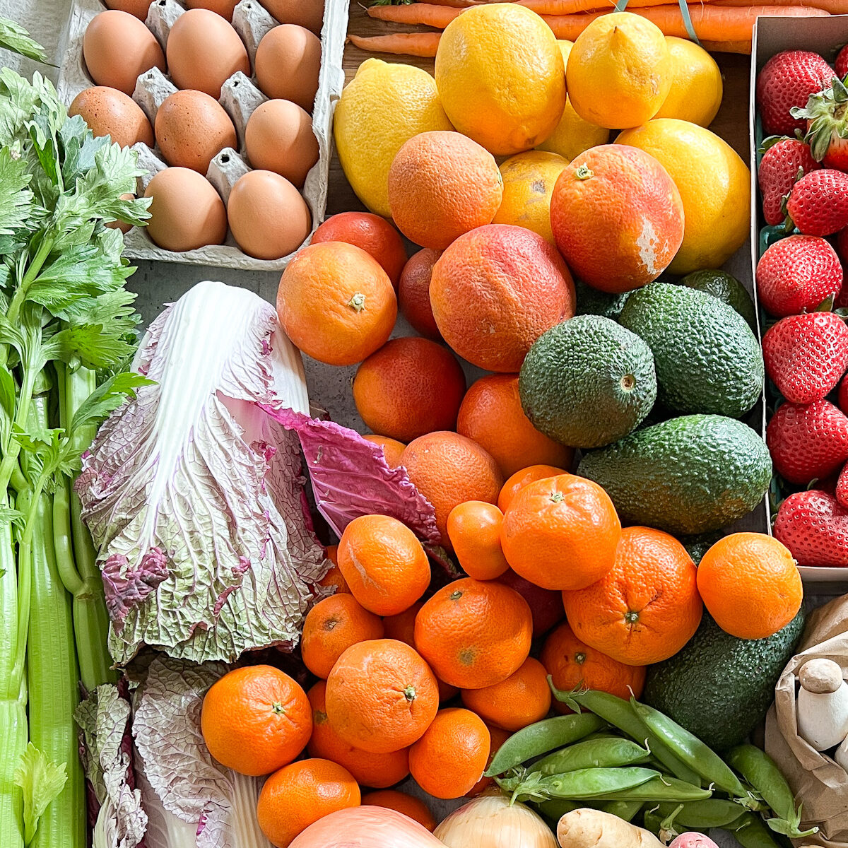 A table full of produce including mushrooms, napa cabbage, potatoes, carrots, and peas.