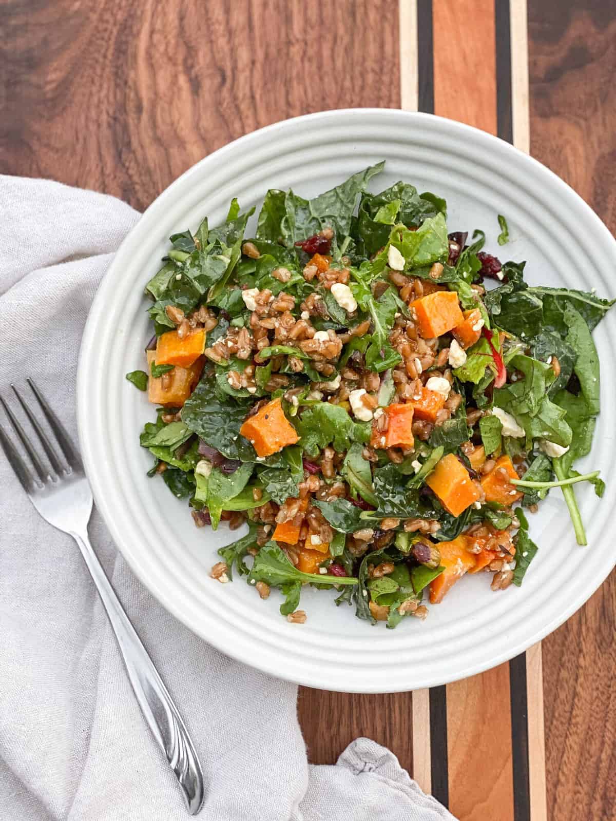 A white bowl holds a salad of mixed beet greens with roasted butternut squash and cooked farro.