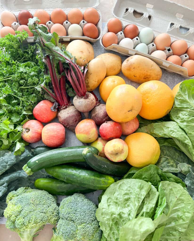 A table of fresh produce laid out for the week to include broccoli, beets, lettuc, apples, and citrus fruits. 