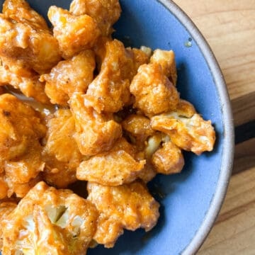 A blue bowl contains saucy buffalo cauliflower.