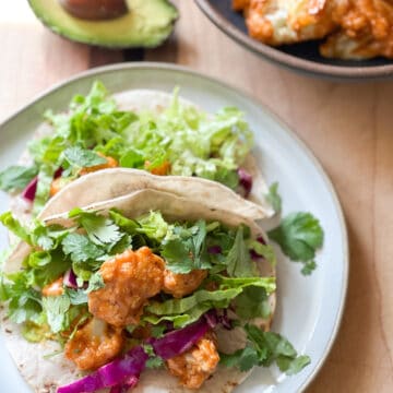 A plate of tacos with buffalo cauliflower bites and shredded lettuce.