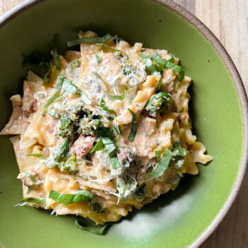 A green pasta bowl holds broken lasagna noodles in a creamy sundried tomato sauce with broccolini.