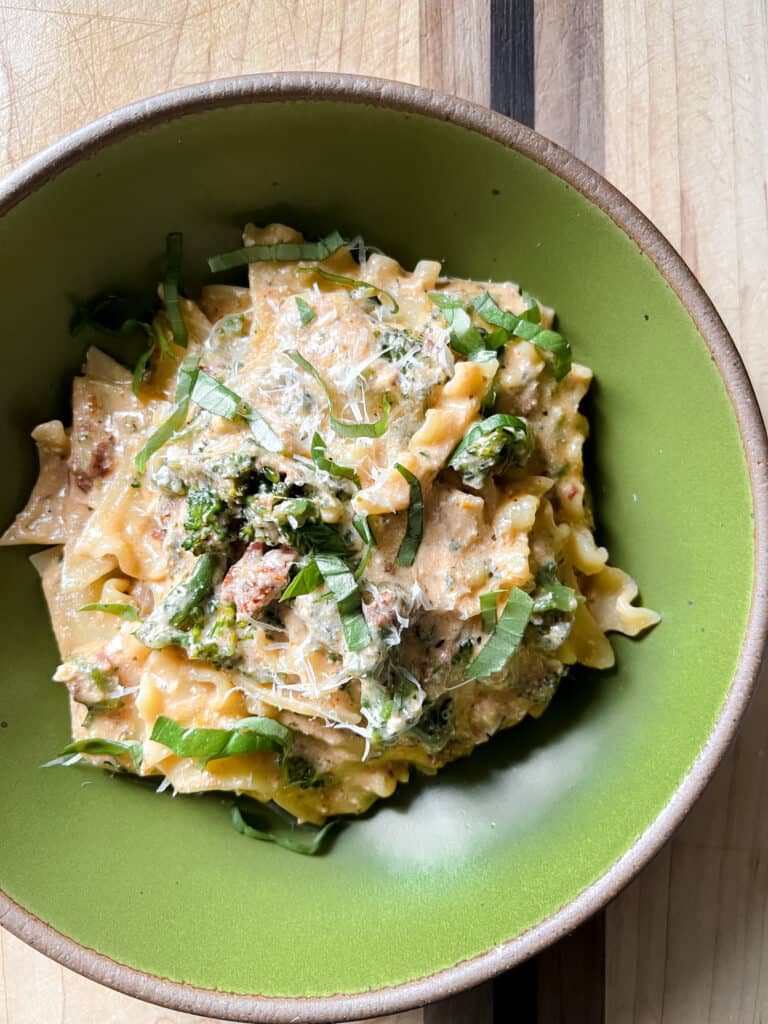 A green pasta bowl holds broken lasagna noodles in a creamy sundried tomato sauce with broccolini.
