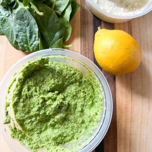 A small bowl of spinach arugula pesto accented with lemon and grated parmesan.