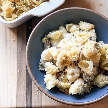 A wooden cutting board hold a bowl of truffle mac and cheese.