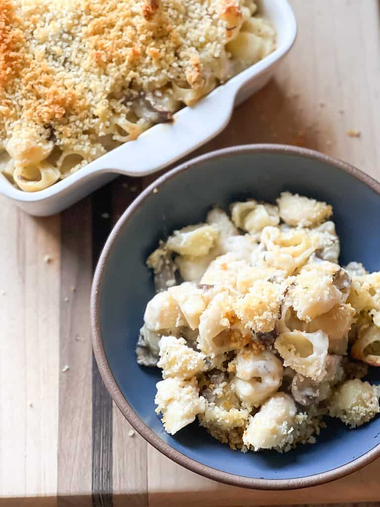 A wooden cutting board hold a bowl of truffle mac and cheese.