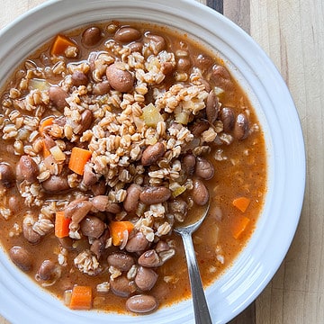 A white bowl holds a generous portion of a vegetable soup with cranberry beans and farro.