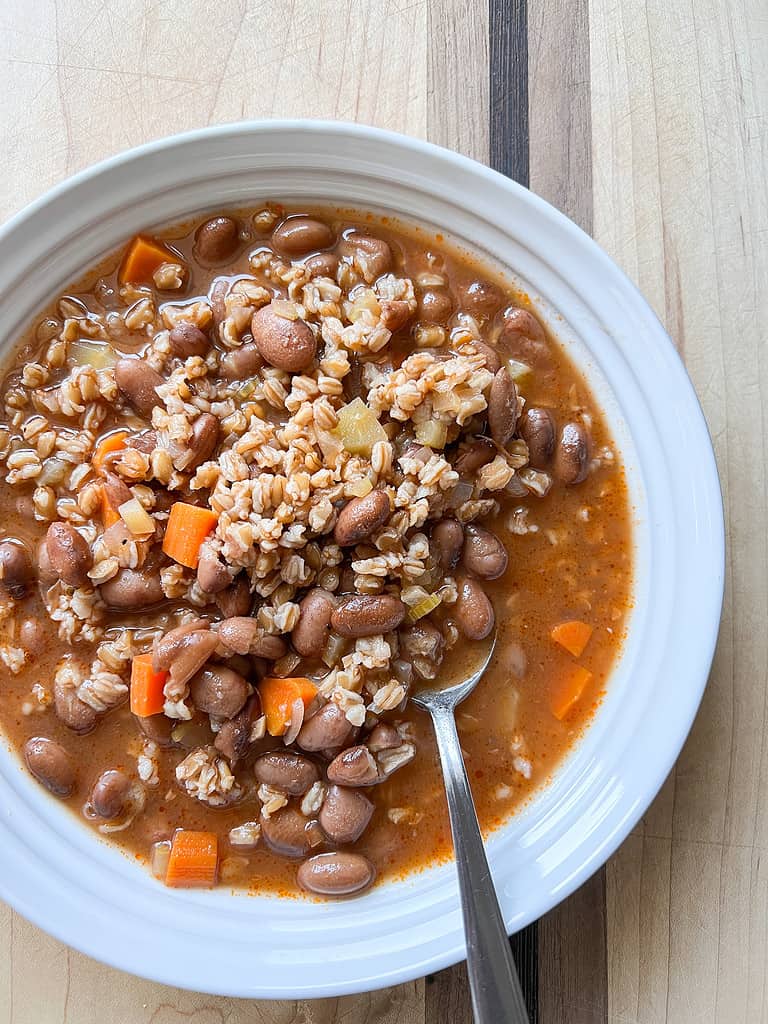 A white bowl holds a generous portion of a vegetable soup with cranberry beans and farro.