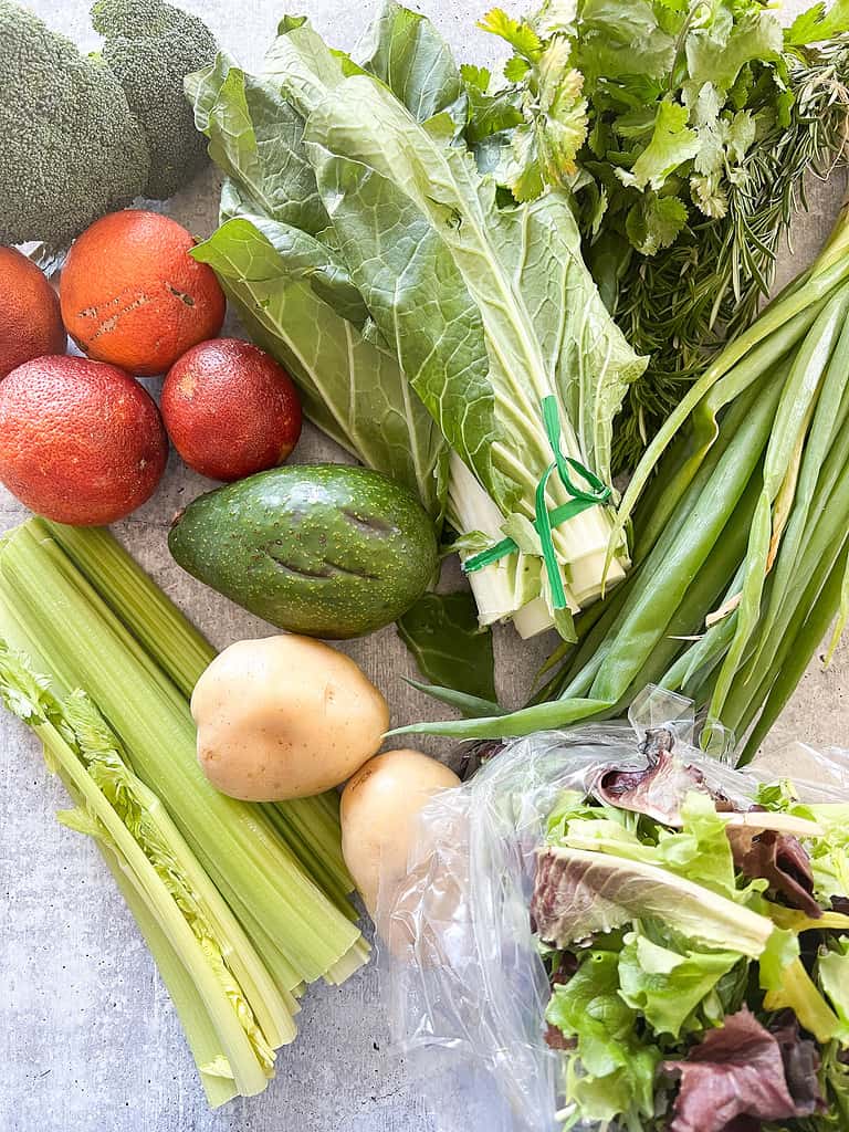 a table full of produce featuring chard, avocado, blood oranges, and mixed greens.