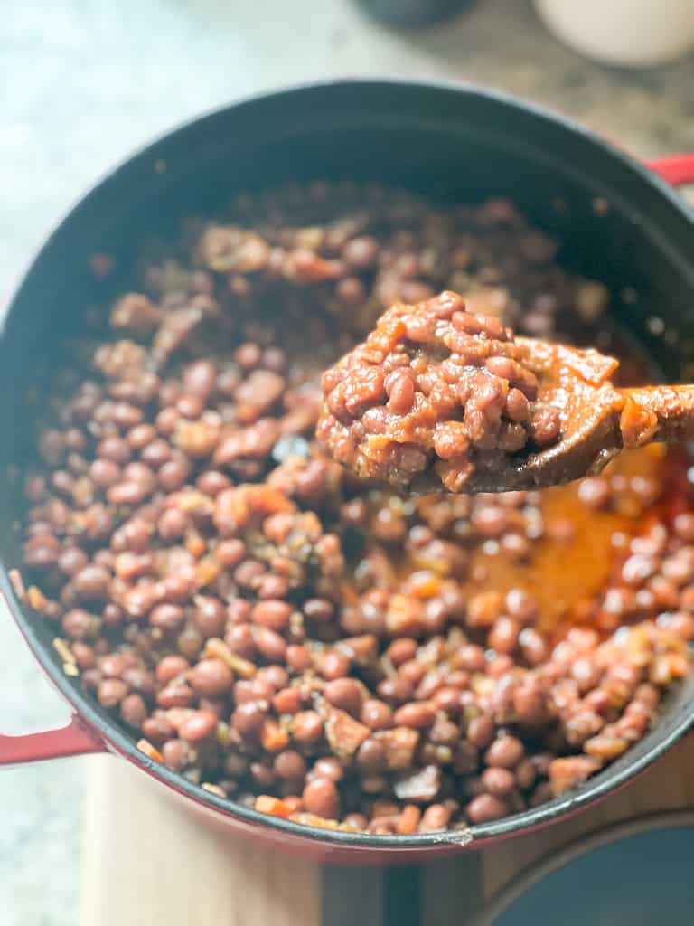 A portrait angle of a spoonful of Stewed Santa Maria-Style Pinquito Beans over the large pot of cooked beans. 