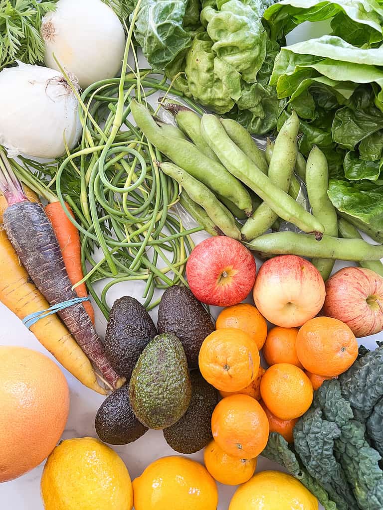 A table full of seasonal vegetables including fava beans, garlic scapes, and romaine lettuce. 