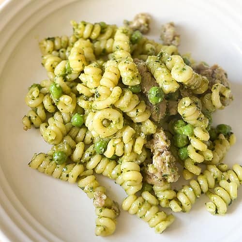 A white pasta bowl holds a serving of Pesto Pasta with Sausage and Peas.