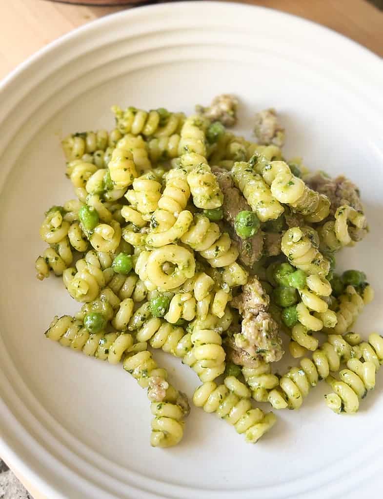 A white pasta bowl holds a serving of Pesto Pasta with Sausage and Peas.
