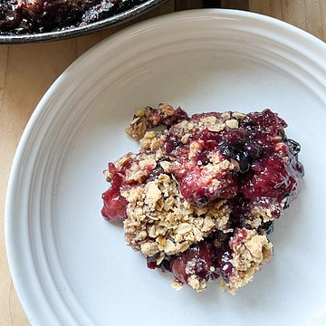 A white bowl holds a few spoonfuls of Easy Cast-Iron Skillet Cherry and Berry Crisp.