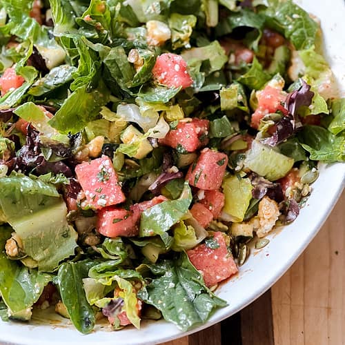 A large white bowl is filled with The Best Watermelon Salad with Easy Chili Lime Dressing.