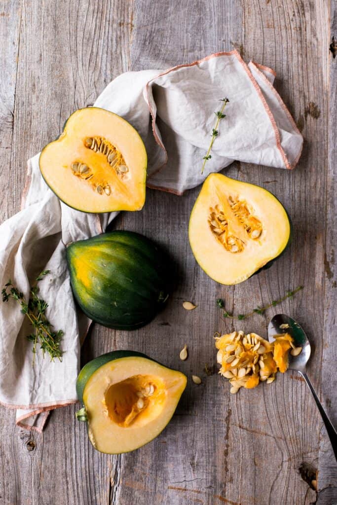 A table is decorated with sliced acorn squash revealing the seeds strewn along a linen kitchen towel.