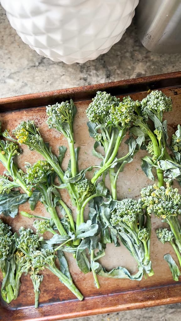 A rimmed baking sheet contains broccolini before roasting.