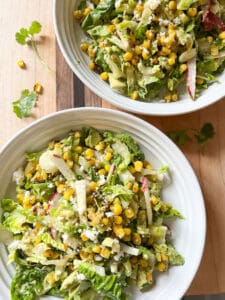 Two white salad bowls hold Charred Corn Salad with Chili Lime Cotija Dressing