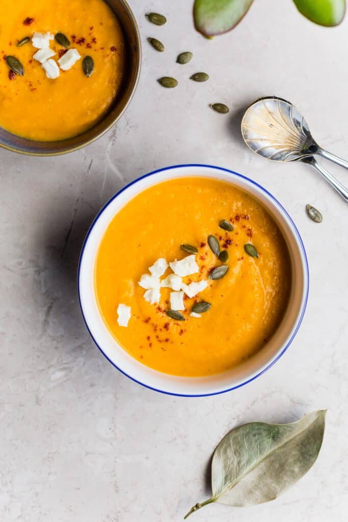 A bowl of butternut squash soup is garnished with toasted pumpkin seeds.