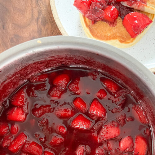 A large saucepan holds a vibrant colored stone fruit compote with peaches, cherries, and plums.