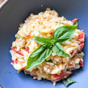 A blue pasta bowl holds a creamy one-pot orzo pasta dish with summertime tomatoes, zucchini, and corn.