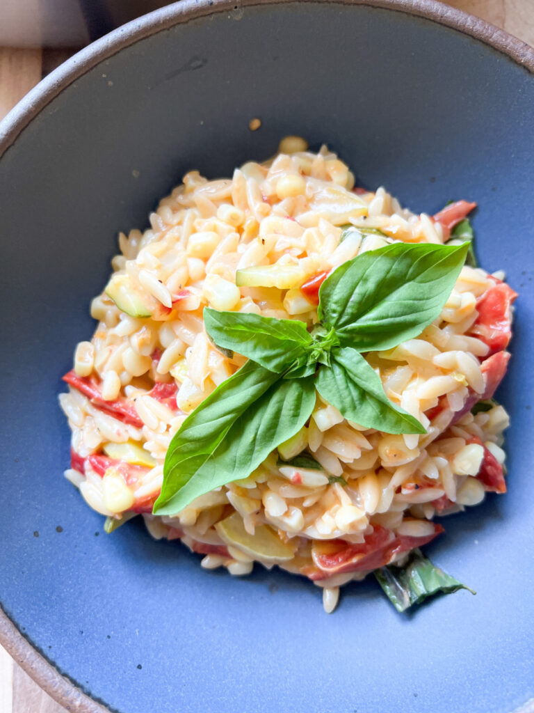 A blue pasta bowl holds a creamy one-pot orzo pasta dish with summertime tomatoes, zucchini, and corn.