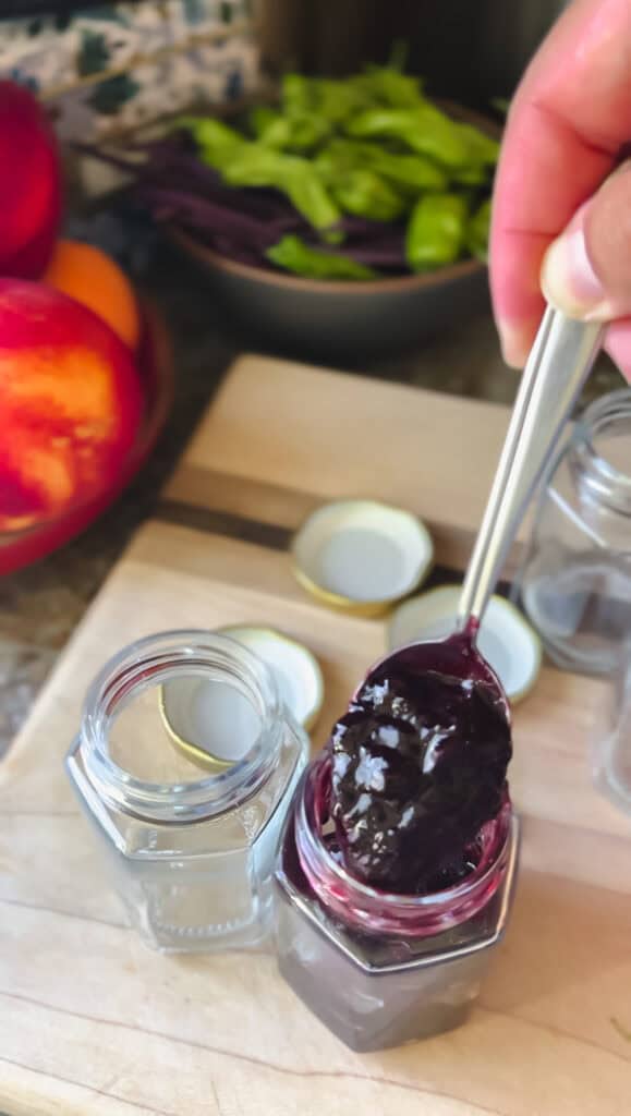 Spooning blueberry butter into a jar to store.