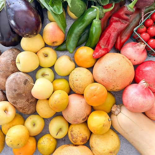A flat lay image contains seasonal produce including eggplant, peppers, and citrus.