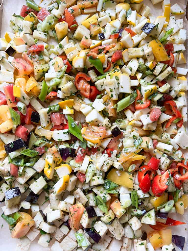 A large sheet pan is filled with late summer vegetables for an Easy Ratatouille dish inspired by the Disney movie of the same name. The tray has an assortment of tomatoes, eggplant, peppers, and onions. 