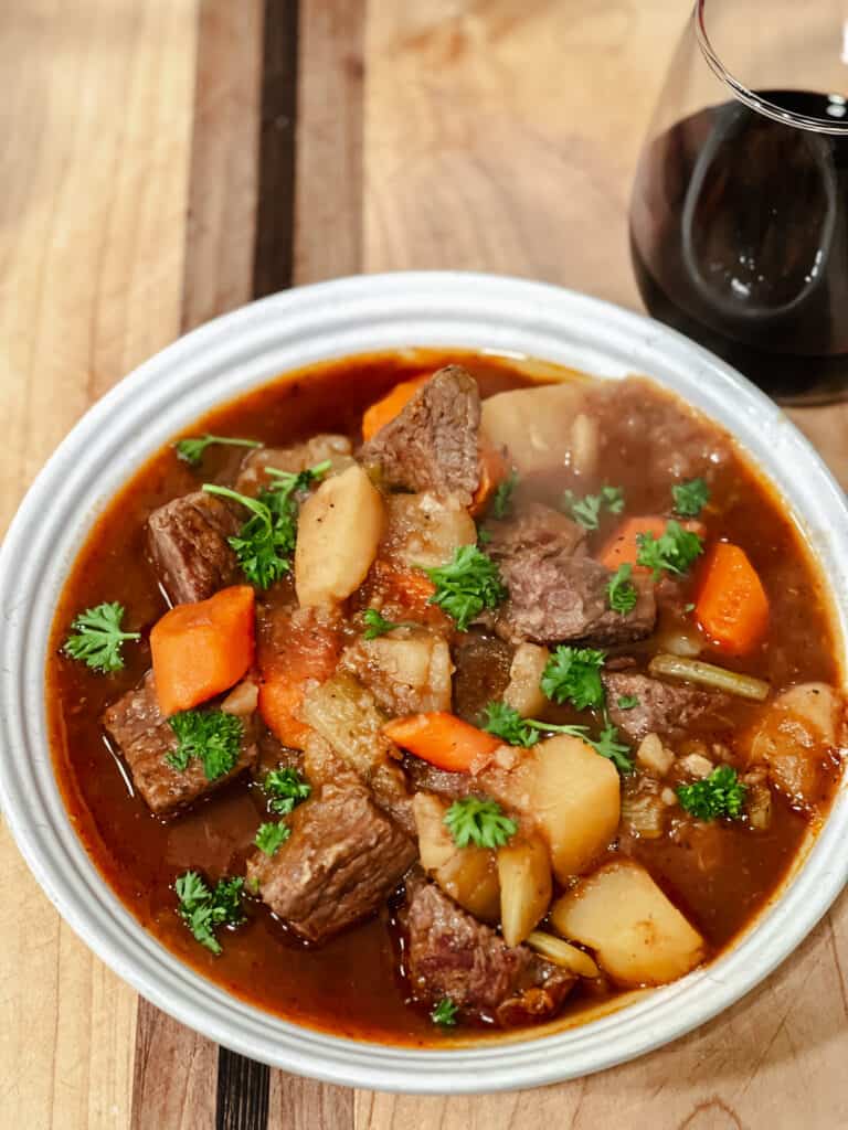 A bright white ceramic bowl cradles a generous portion of an Easy One Pot Classic Beef Stew complete with tender beef chunks, carrots, potatoes, celery, and beef broth.