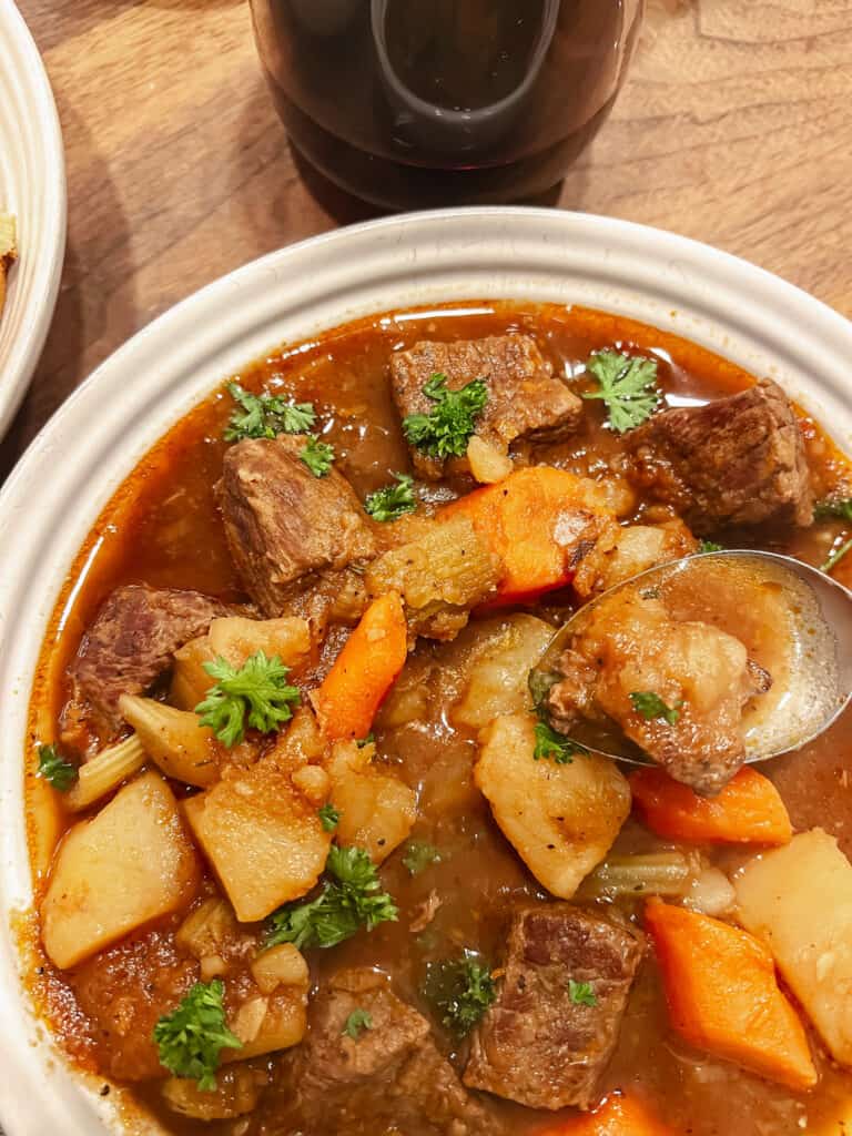 A bright white ceramic bowl cradles a generous portion of an Easy One Pot Classic Beef Stew complete with tender beef chunks, carrots, potatoes, celery, and beef broth.