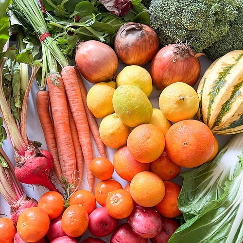 A flatlay image of fresh winter produce features beets, carrots, chard, squash, citrus, and red potatoes.