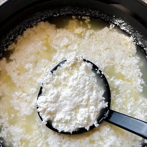 Homemade cottage cheese in a pot with a ladle lifting up a serving.