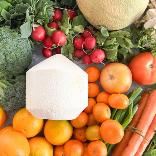A flatlay image of seasonal produce featuring coconut, carrots, spring citrus, and fava bean greens.