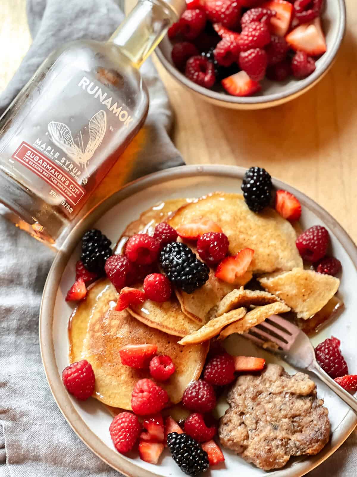 A plate of banana pancakes on a plate with a sausage patty and fresh berries.