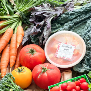 Portrait shot of autumnal produce for Dinner Plans Week 46 featuring kale, mustard greens, carrots, tomatoes, cabbage, spinach, arugula, and Daikon radish kimchi.