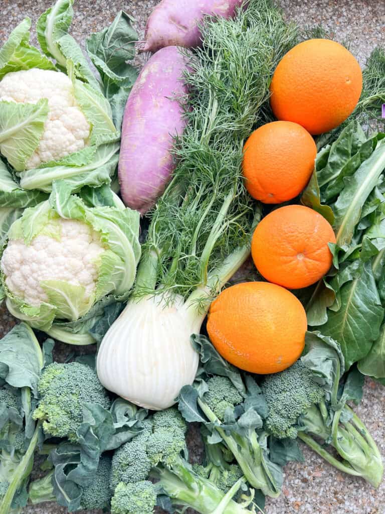 Flat lay photo for Dinner Plans Week 5 featuring Navel oranges, purple daikon radish, two heads of cauliflower, dandelion greens, fennel, and broccoli.