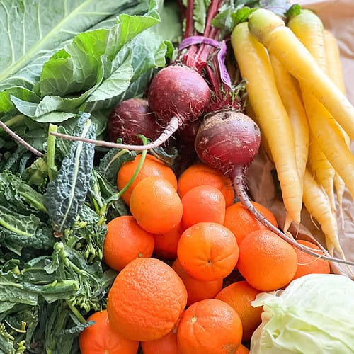 Portrait image of late winter produce for Dinner Plans Week 10 featuring red beets, yellow carrots, cabbage, mandarins, dino rabe, and collard greens.