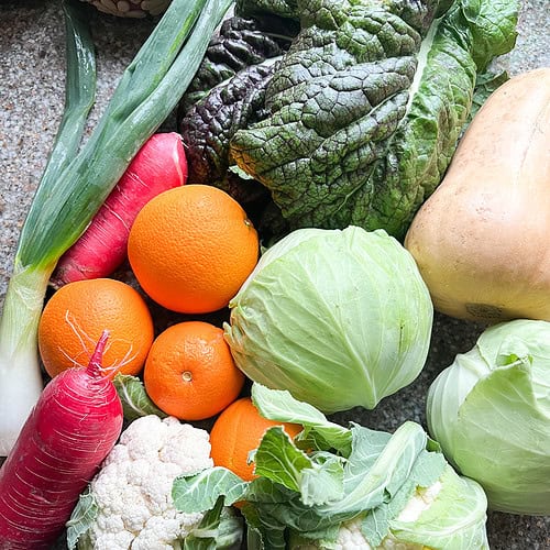 A flatlay photo of winter produce for Dinner Plans Week 7 featuring cabbage, cauliflower, mustard greens, butternut squash, Navel oranges, and spring onion.