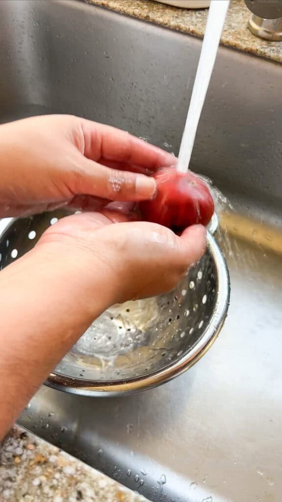 Two brown hands are shown gently rinsing heirloom tomatoes for storing in freezer. 