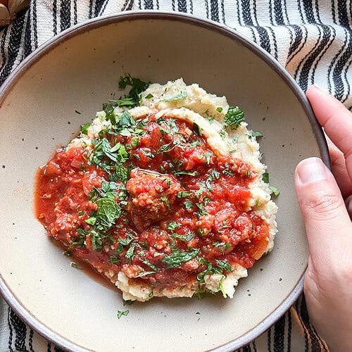 Portrait photo of 30 Minute Lamb Ragu generously served over a bed of roast cauliflower puree.
