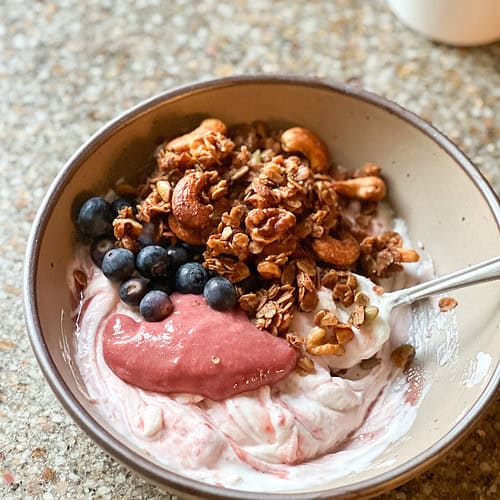 Portrait shot of blood orange curd dollops in plain greek yogurt. Topped with granola and blueberries.