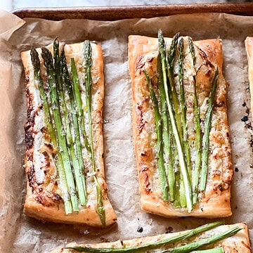 Portrait photo of prepared Asparagus Tart with Puff Pastry freshly baked to golden brown and crispy. Asparagus spears have been roasted in a creme fraîche flavored with caramelized shallot and spring onion.
