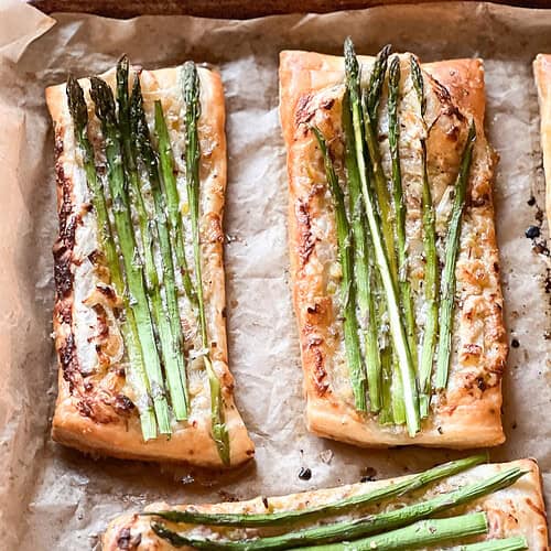 Portrait photo of prepared Asparagus Tart with Puff Pastry freshly baked to golden brown and crispy. Asparagus spears have been roasted in a creme fraîche flavored with caramelized shallot and spring onion.