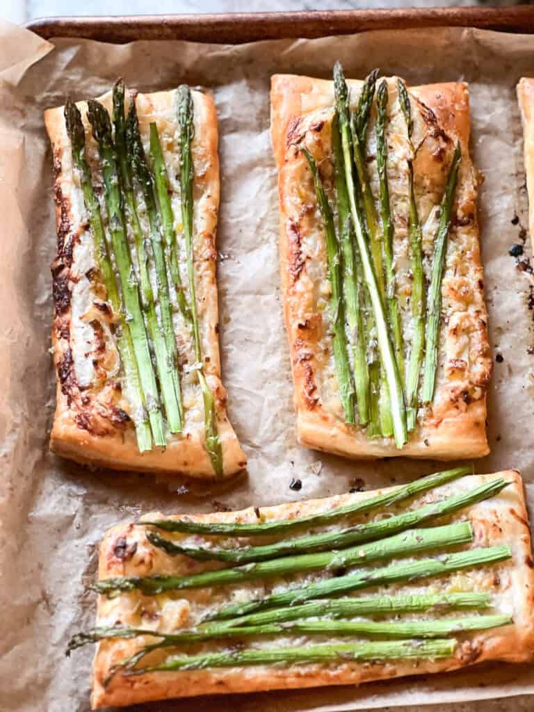 Portrait photo of prepared Asparagus Tart with Puff Pastry freshly baked to golden brown and crispy. Asparagus spears have been roasted in a creme fraîche flavored with caramelized shallot and spring onion. 